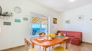A dining area with a table set for two, a red sofa, and a view of the sea through a glass door. - Apartments Ivan Sea View Lun (Lun)