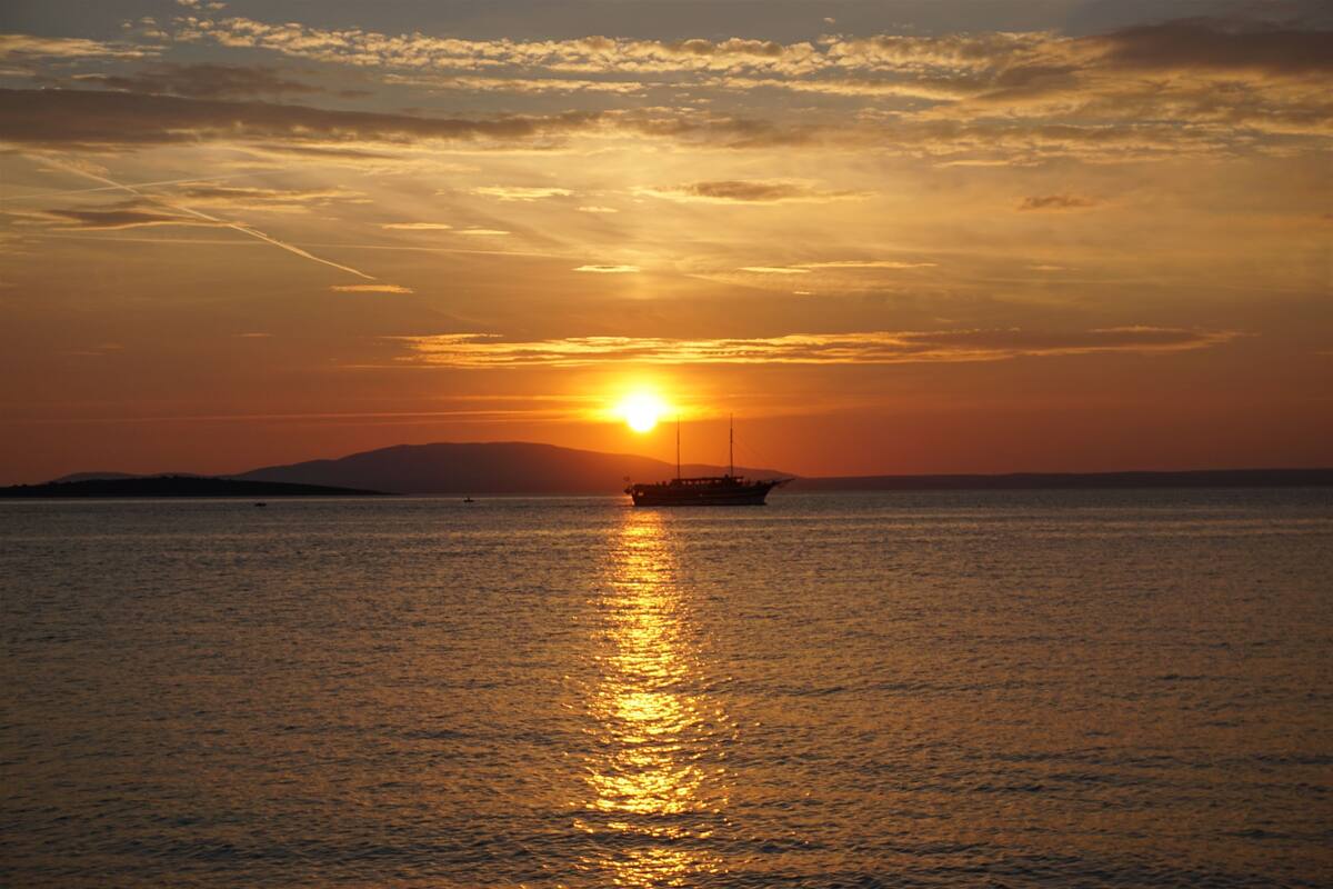 Un coucher de soleil sur une mer calme, avec un bateau à l'horizon.