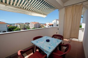 Un balcon avec une table et des chaises, une vue sur les maisons et un auvent à rayures.