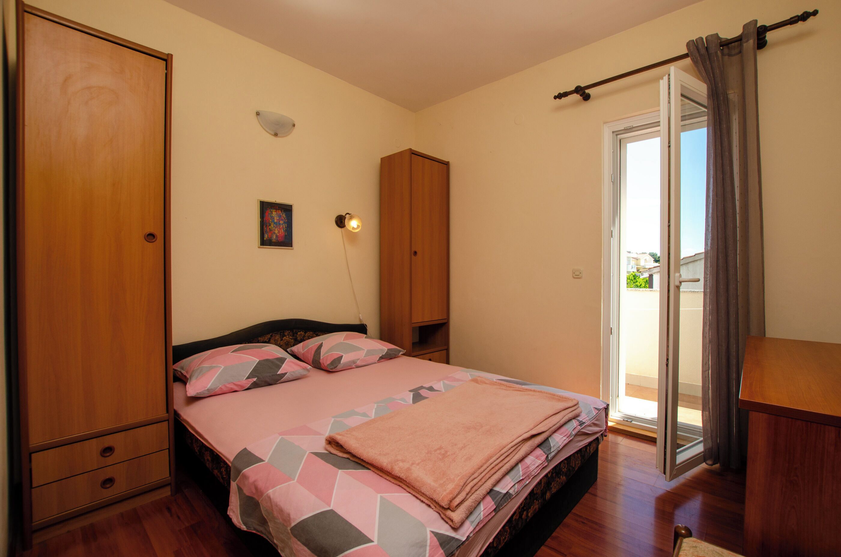 A bedroom with a bed, a wardrobe, a desk, a chair, and a sliding glass door to the outside.