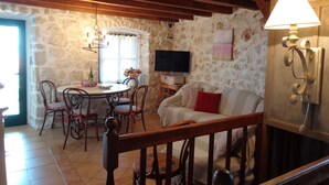 Una stanza rustica con parete in pietra, travi in legno, un tavolo rotondo con sedie, un divano e una televisione.