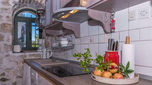 Una cucina con parete in pietra, un piano di lavoro in legno, una pianta in vaso e un bollitore rosso.