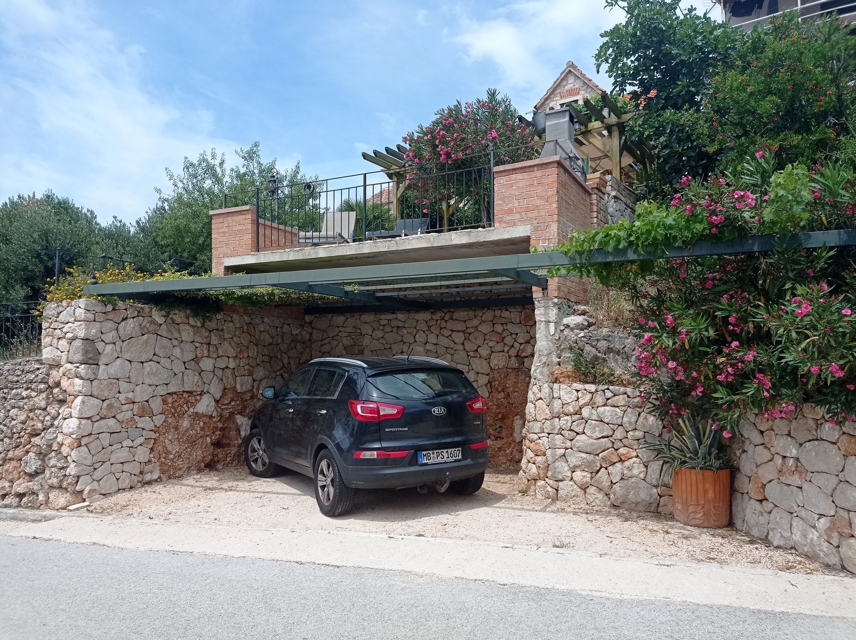 Ein schwarzer SUV parkt in einer überdachten Tiefgarage mit Steinmauern und einem Backsteinhaus im Hintergrund.