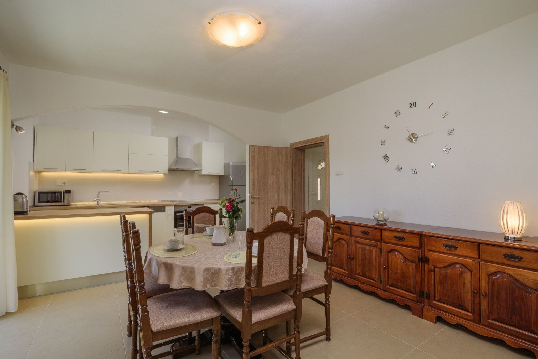A modern kitchen with white cabinets, a dining table with chairs, and a wooden cabinet with drawers.