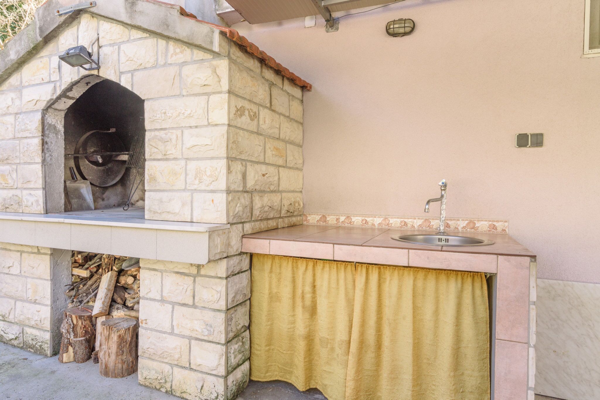 Un horno de piedra exterior con chimenea de ladrillo, un lavamanos y una cortina amarilla.