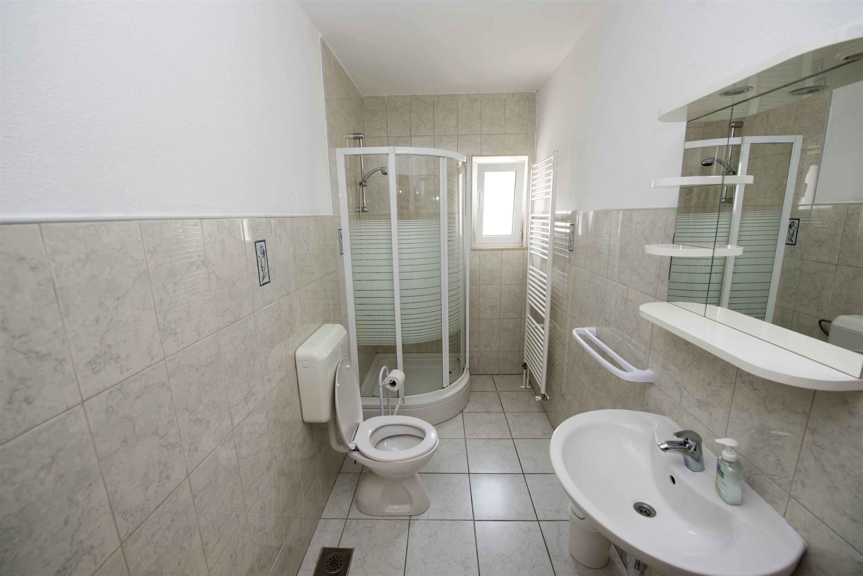 A bathroom with a toilet, shower, sink, and mirror.