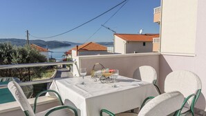 Un balcon avec une table dressée pour deux personnes, donnant sur un plan d’eau et des collines.