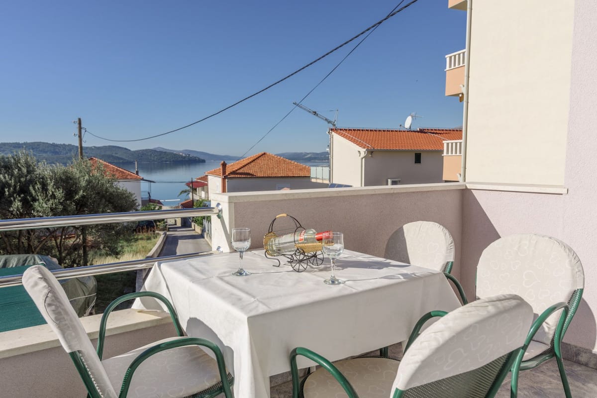 A balcony with a table set for two, overlooking a body of water and hills.