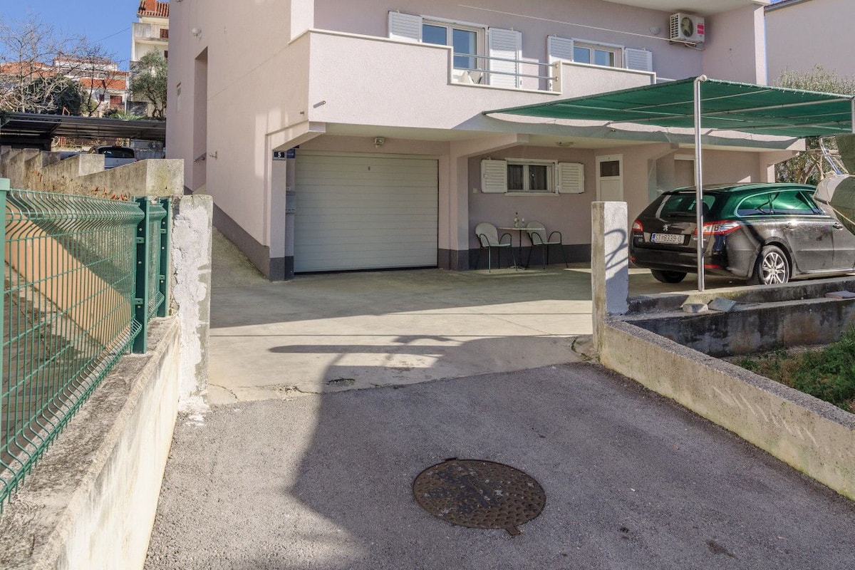 A multi-story residential building with a garage, outdoor seating area, and a car parked in front.