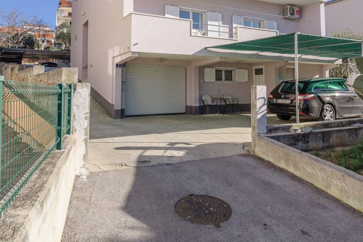 A multi-story residential building with a garage, outdoor seating area, and a car parked in front.