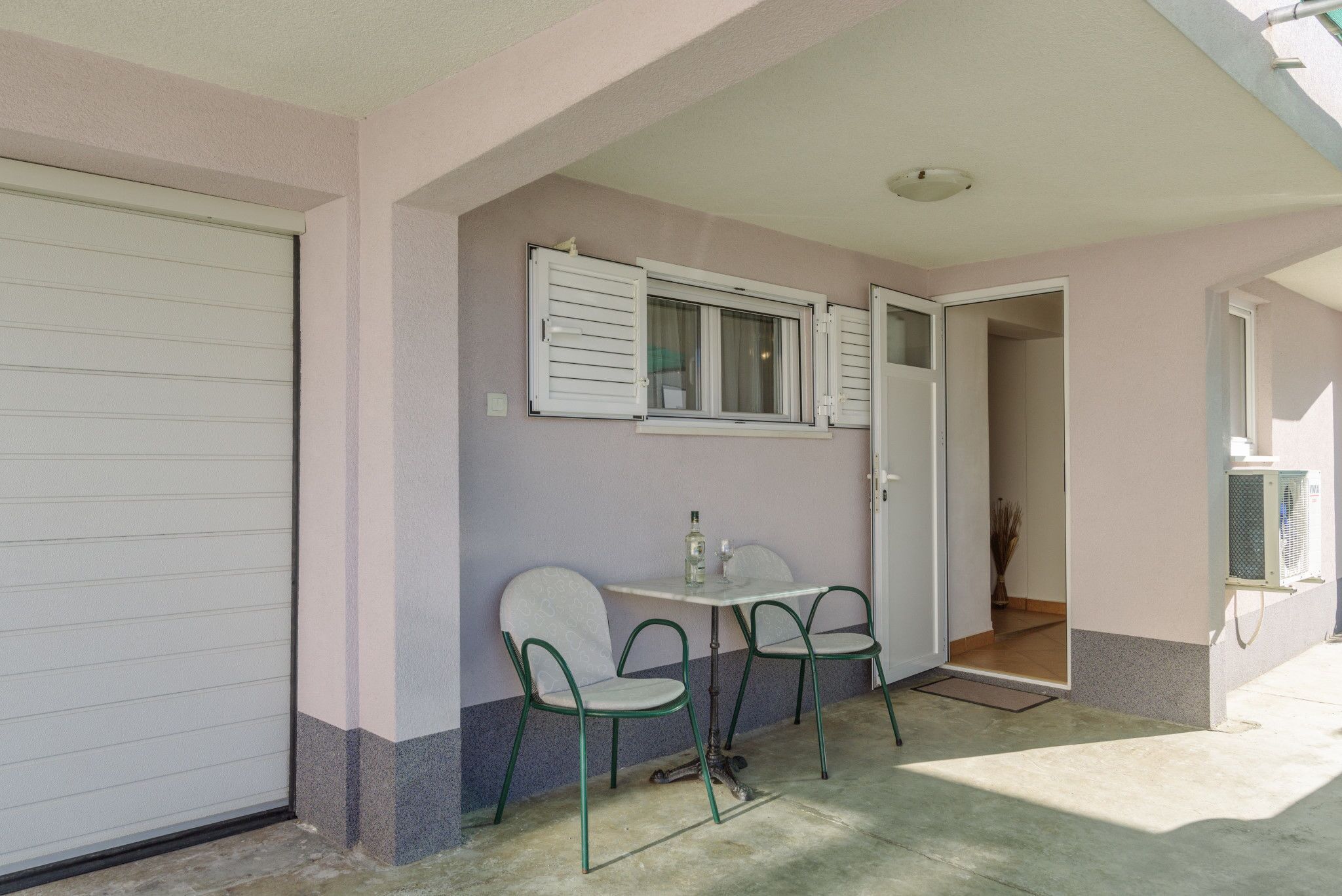 A small patio with a table and two chairs, a sliding door, and a window with shutters.