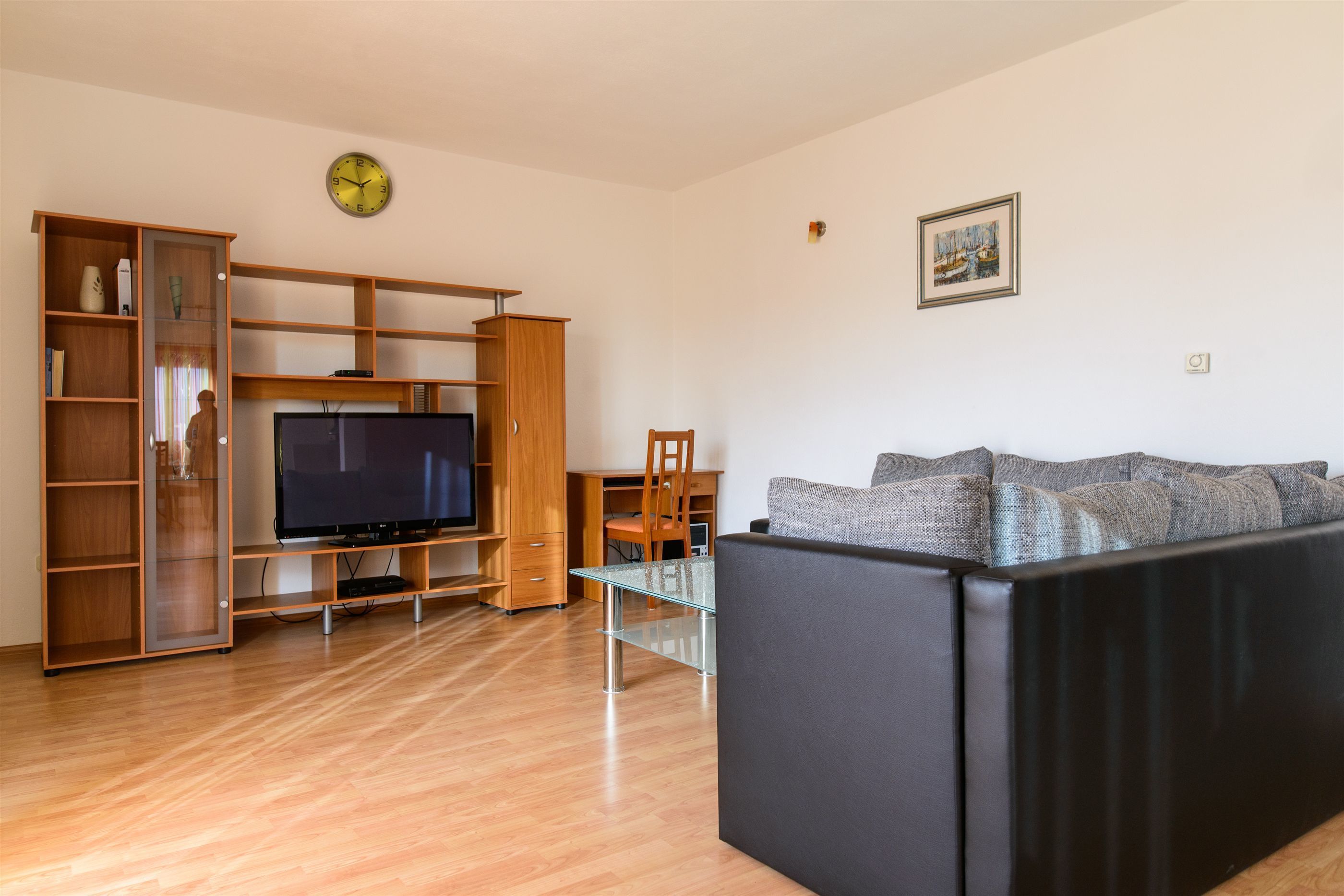 A living room with a flat-screen TV, wooden entertainment unit, and a black sofa.