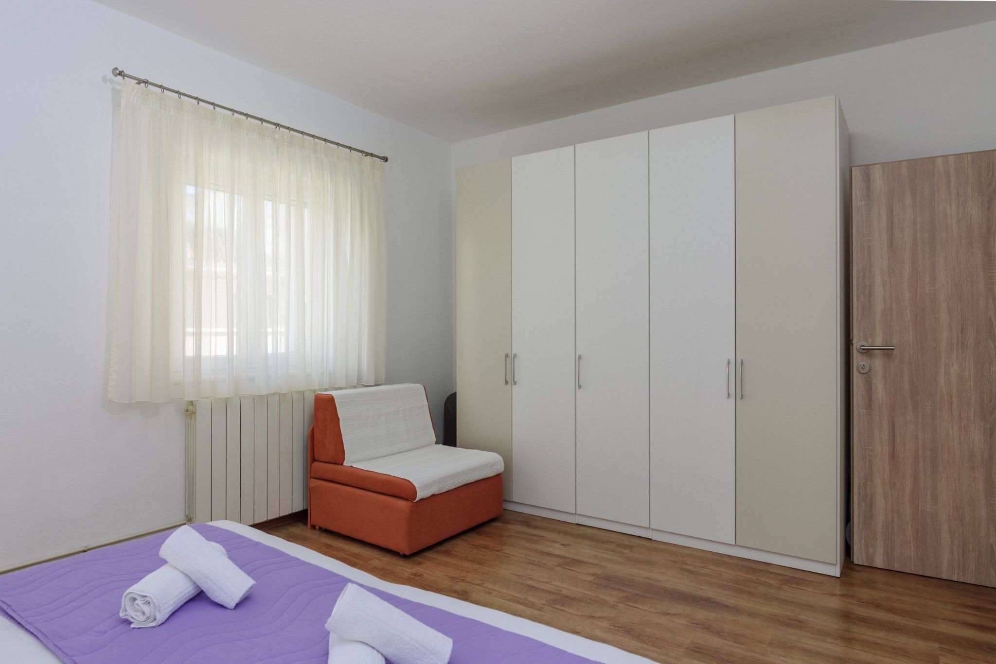 A bedroom with a bed, a chair, a wardrobe, and a door.
