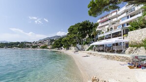 Una playa con agua cristalina, un muro de piedra y un restaurante con terraza.