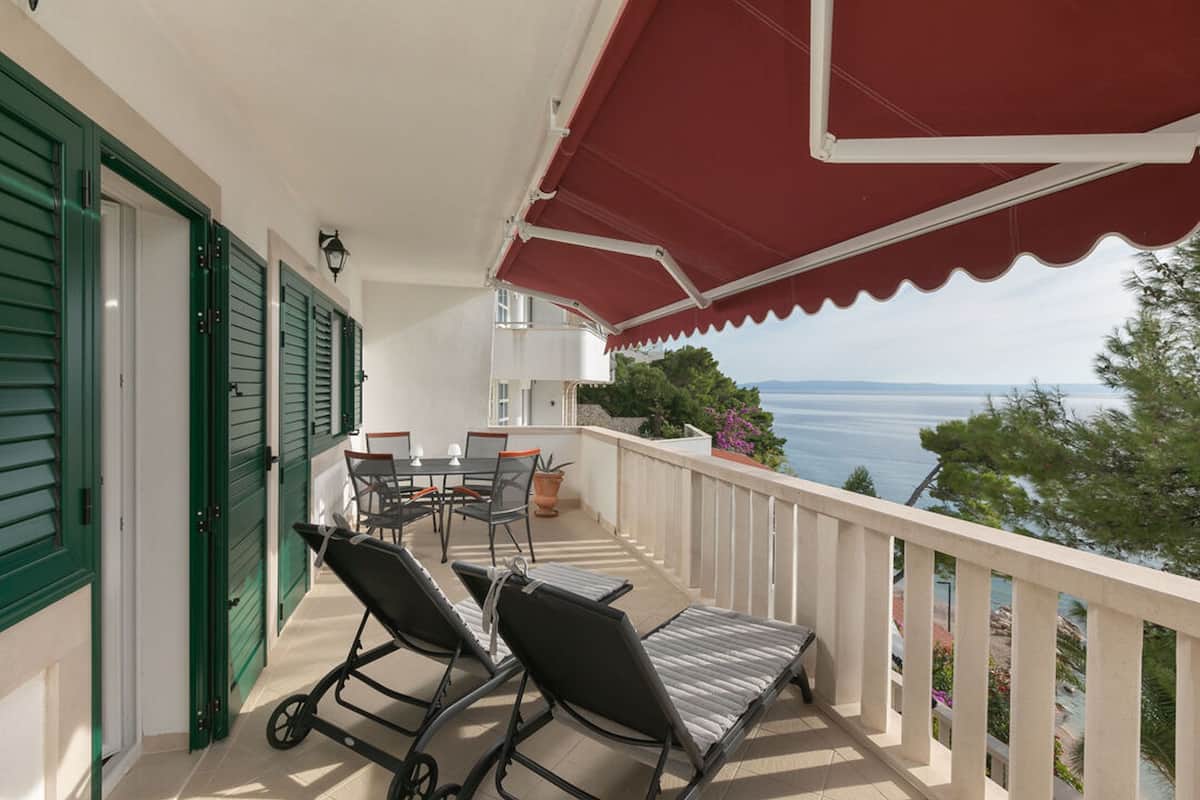 A balcony with two lounge chairs, a table, and chairs, overlooking a scenic view of the sea.