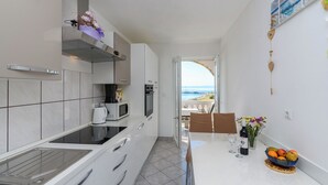A modern kitchen with a view of the sea, a dining area with a table set for two, and a small fruit bowl on the counter. - Apartments Albina (Lopar)