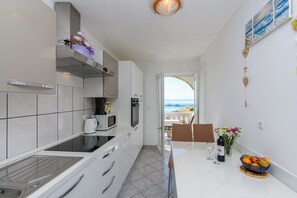 A modern kitchen with a view of the sea, a dining area with a table set for two, and a small fruit bowl on the counter. - Apartments Albina (Lopar)