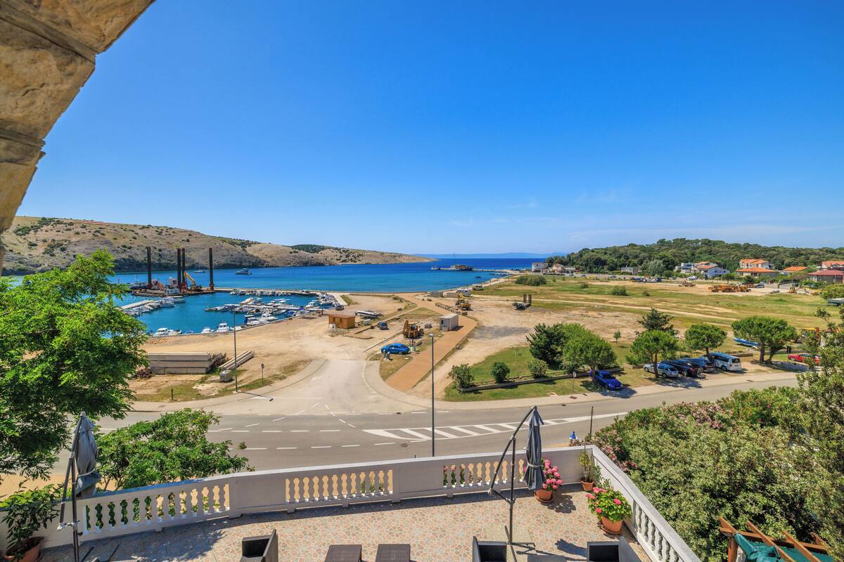 A coastal view with a marina, clear skies, and a road leading to a residential area.