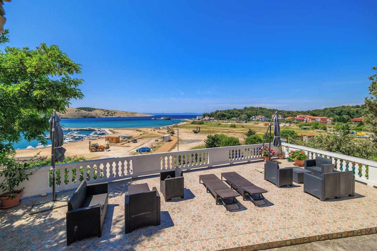 A terrace with outdoor seating, a view of the sea, and a distant landscape.