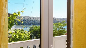 A balcony with a view of a lake, trees, and a hilly landscape. - Apartments Albina (Lopar)