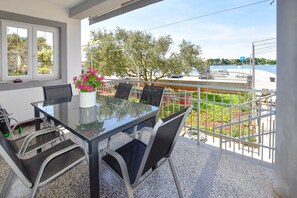 A balcony with a glass table and chairs, a vase of flowers, and a view of the sea and trees.