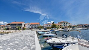 A marina with boats docked, a paved walkway, and buildings with red roofs. - Apartment Danica (Sukosan)
