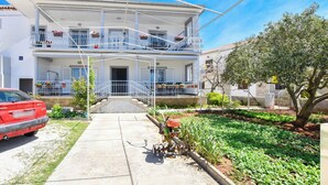 A two-story building with a balcony on the upper floor, a garden in the front yard, and a parked car. - Apartment Danica (Sukosan)