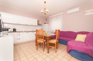 A compact kitchen with white cabinets, a dining table with chairs, and a purple sofa. - Apartment Danica (Sukosan)