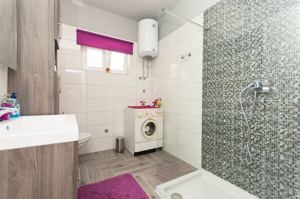 A compact bathroom with a washing machine, a toilet, a sink, and a shower area.