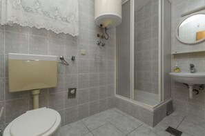 Une salle de bain équipée de toilettes, d’un lavabo, d’une douche et d’un miroir.