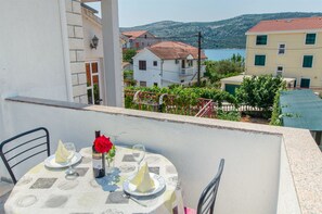 Un balcon avec une table dressée pour deux personnes, une bouteille de vin et un vase contenant une rose.
