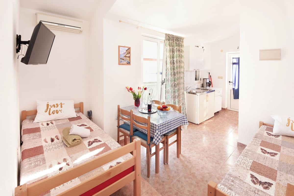 A cozy room with a bed, a small table with chairs, a kitchen area, and a bathroom.