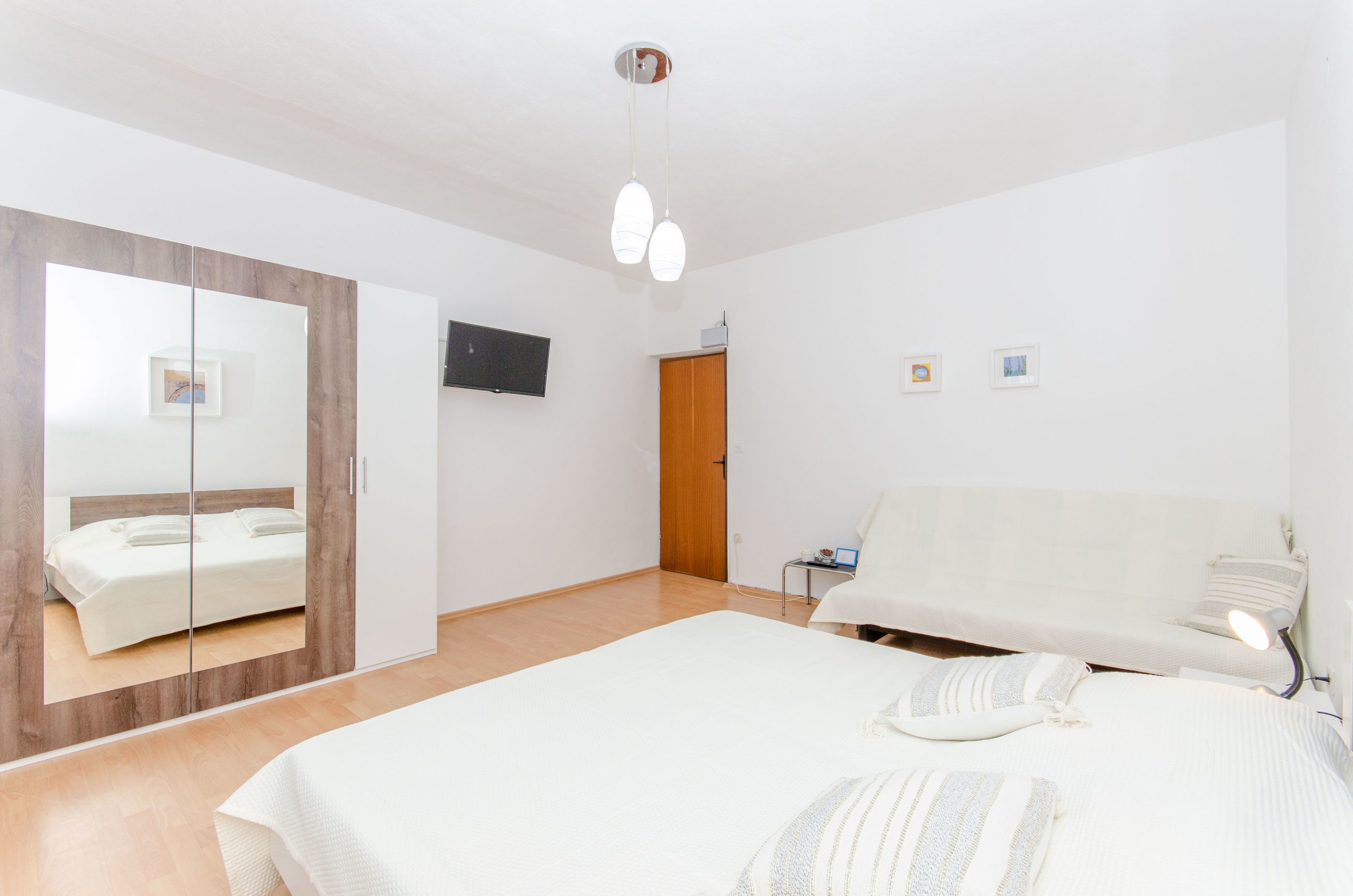 Un dormitorio moderno con una cama grande, un armario con espejo, un televisor en la pared y una puerta de madera.