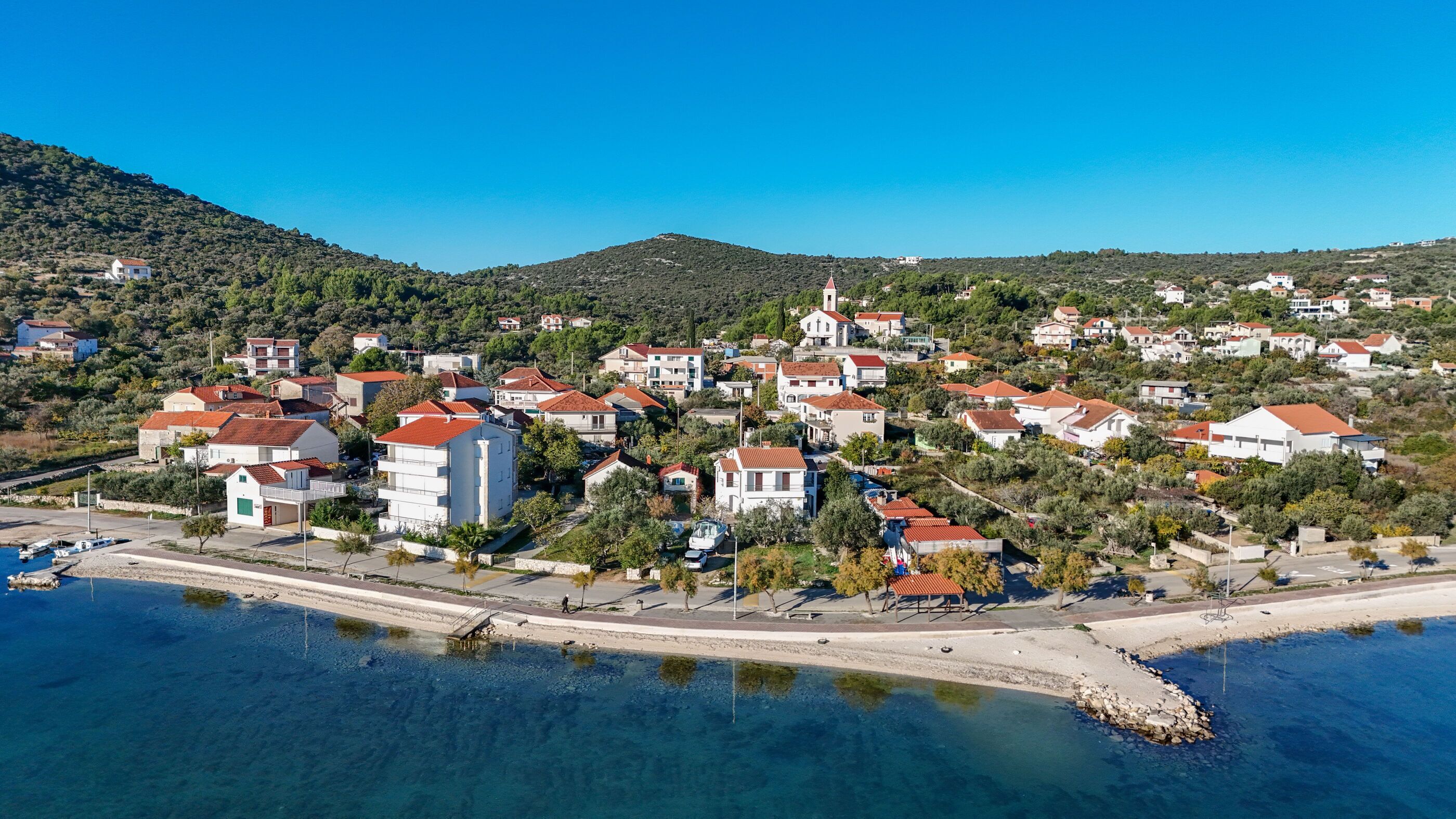 A coastal town with buildings, a church, and clear blue waters.