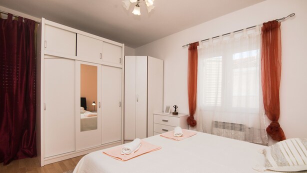 Ein Schlafzimmer mit Bett, Schrank, Nachttisch und einem Fenster mit Vorhängen.