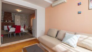Ein Wohnzimmer mit einer Couch, ein Essbereich mit Tisch und Stühlen sowie eine Küche mit Kühlschrank und einer Ziegelwand.