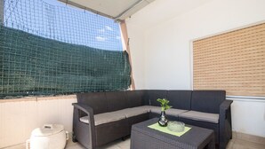 Ein Balkon mit einem Rattan-Sofa, einem kleinen Tisch und einer Topfpflanze.