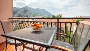 A balcony with a table and chairs, a bowl of fruit, and a view of mountains and buildings. - Apartments Zecic (Omis)
