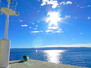 A clear sky with the sun shining over a body of water, a lamp post, and a distant shoreline. - Apartments Zecic (Omis)