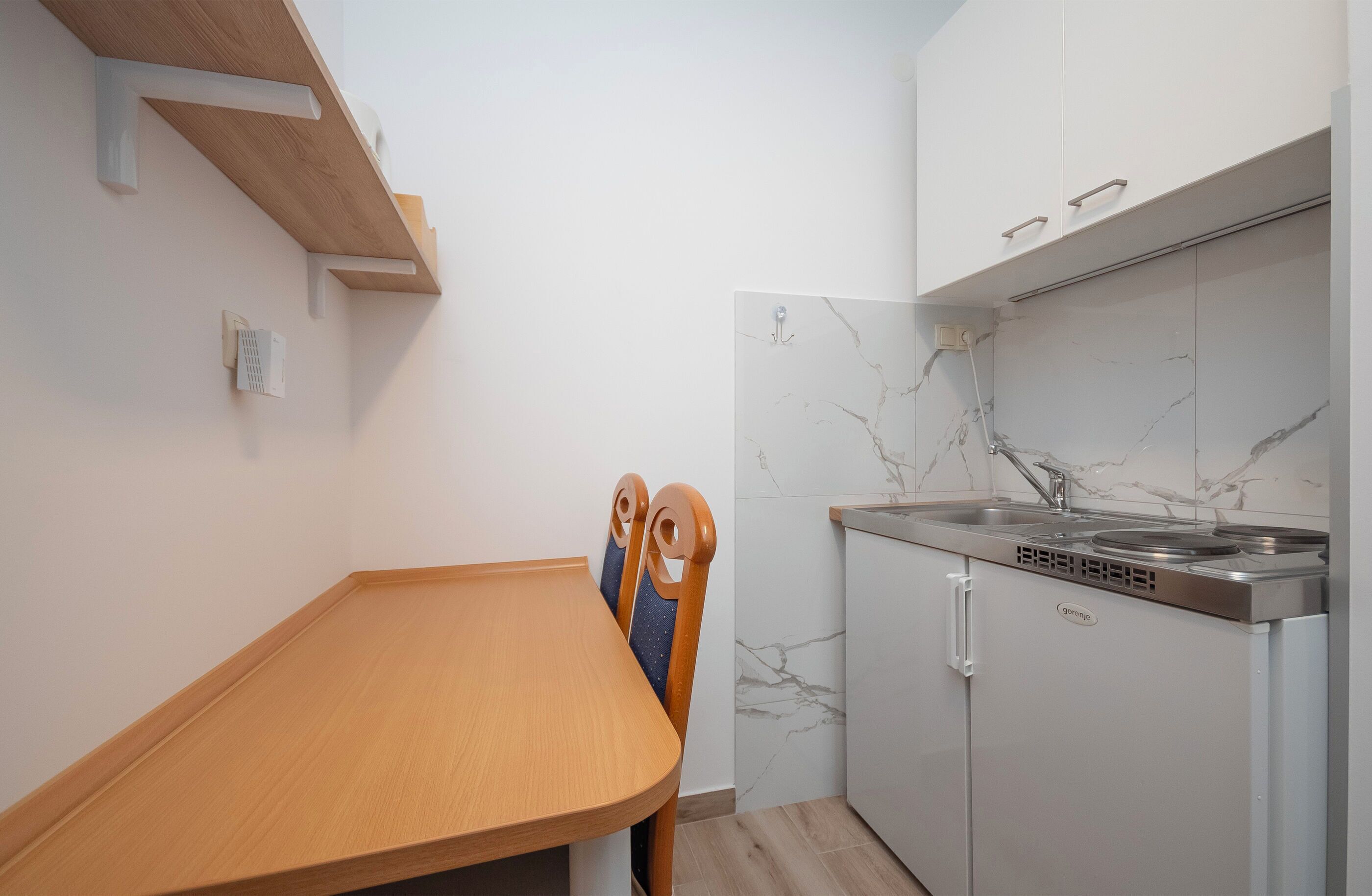 Una cocina compacta con estufa integrada, armarios blancos y una mesa de comedor de madera.