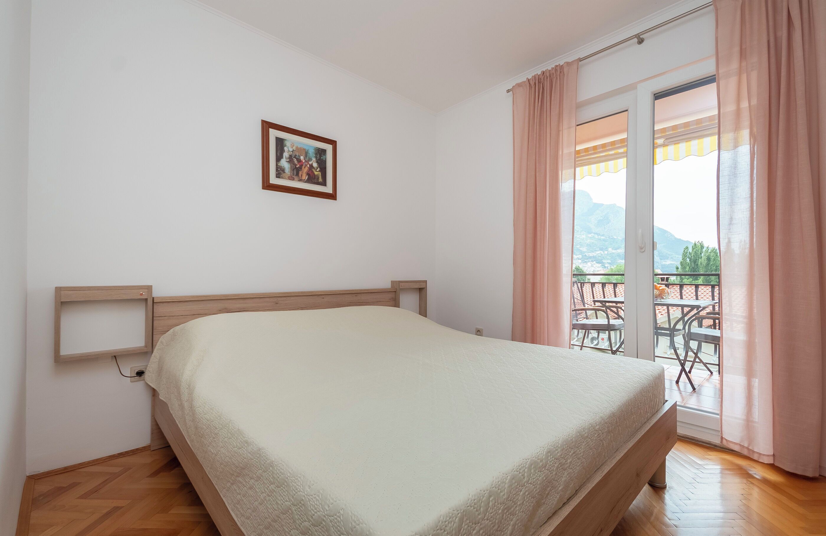 Une chambre à coucher avec un lit, un tableau accroché au mur et un balcon avec des rideaux.