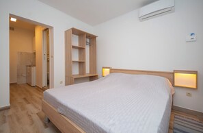 A bedroom with a wooden bed, built-in shelving, an air conditioner, and bedside lamps. - Apartments Zecic (Omis)