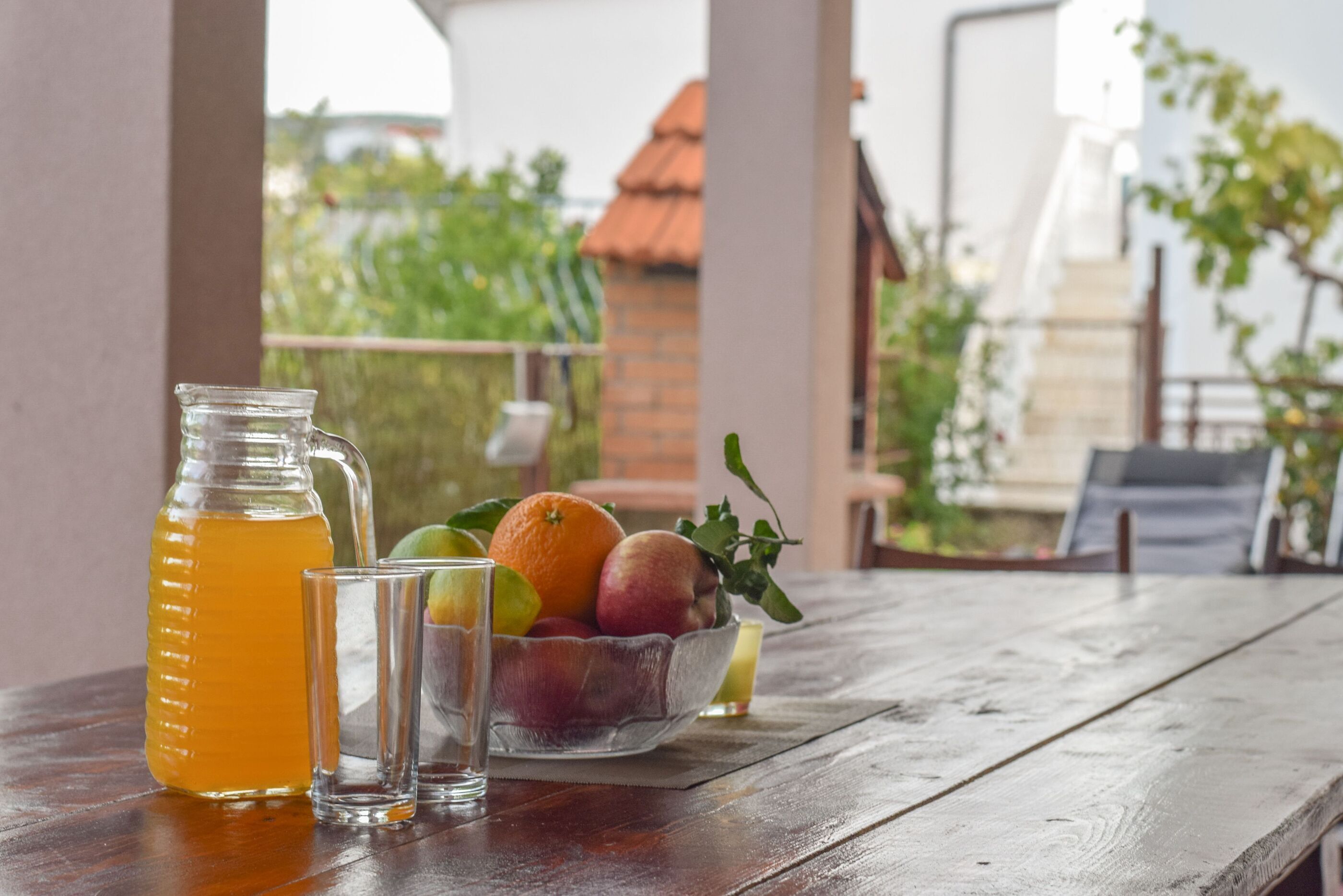 A wooden table with a pitcher of orange juice, two glasses, and a bowl of fruit.