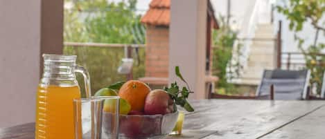 A wooden table with a pitcher of orange juice, two glasses, and a bowl of fruit.