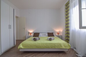 A neatly made bed with a green bedspread, two pillows, and two rolled towels on the bed.