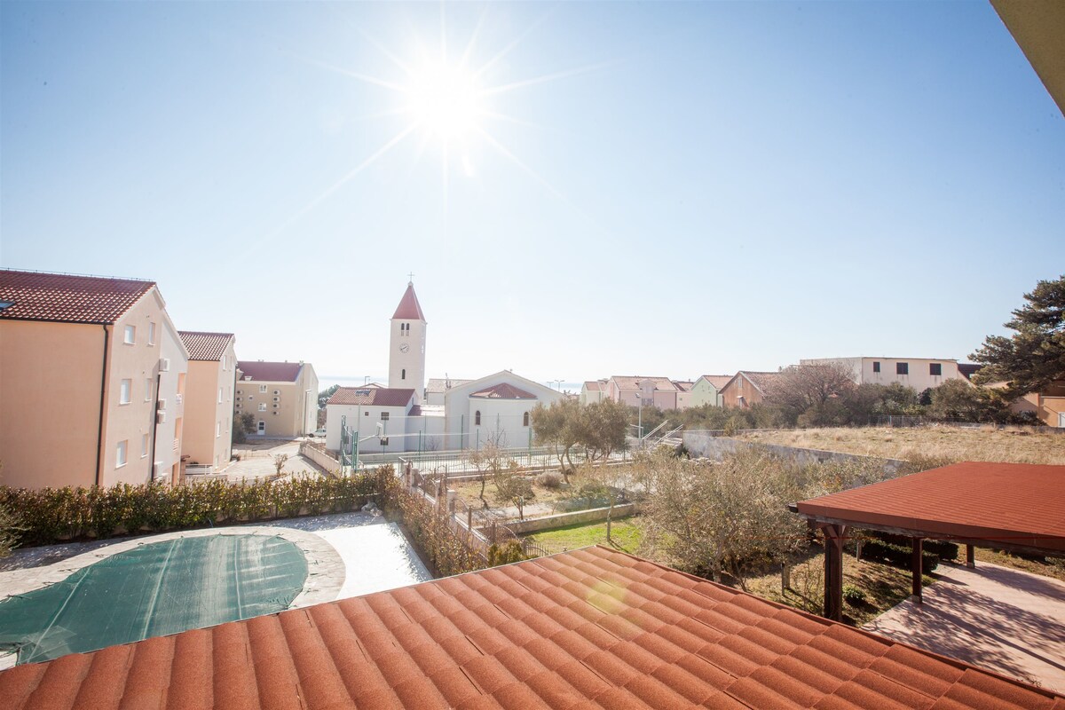 A residential area with a prominent church tower, a tennis court, and a covered outdoor seating area.