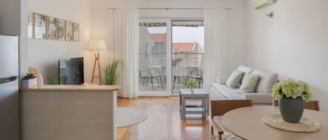 Sala de estar moderna com sofá, mesa de centro e mesa de jantar. Há uma televisão, um abajur e um vaso de plantas.