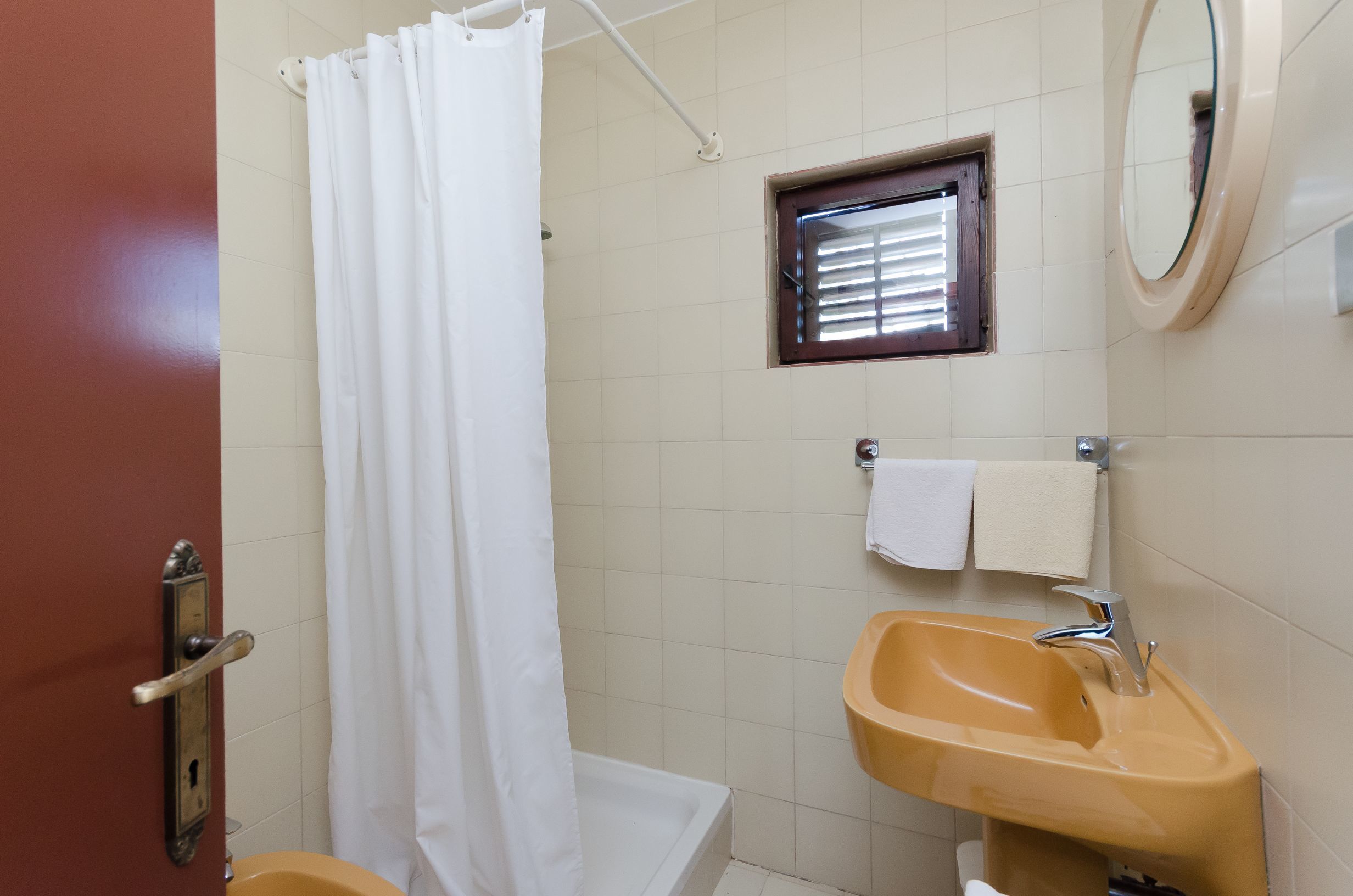 A bathroom with a white shower curtain, a small window, a sink with a mirror, and a towel rack.