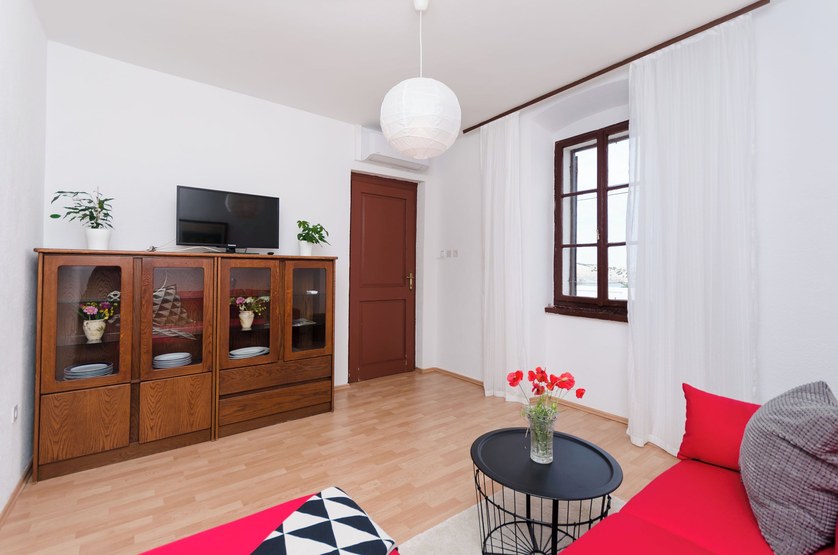 Un salon moderne avec un meuble en bois, un téléviseur à écran plat, une table basse ronde ornée d’un vase de fleurs et un canapé rouge.