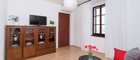 Un salon moderne avec un meuble en bois, un téléviseur à écran plat, une table basse ronde ornée d’un vase de fleurs et un canapé rouge.